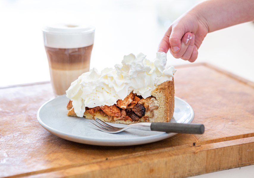 Persoon steekt vinger in slagroom op appeltaart op schotel met vork, met koffie op achtergrond